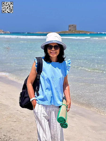 Italy Stintino La Pelosa beach woman wearing a sun hat with a beach mat.