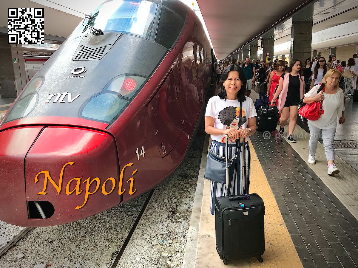 Italy Naples Napoli Centrale, women with luggage standing next to a red high speed train at the station.