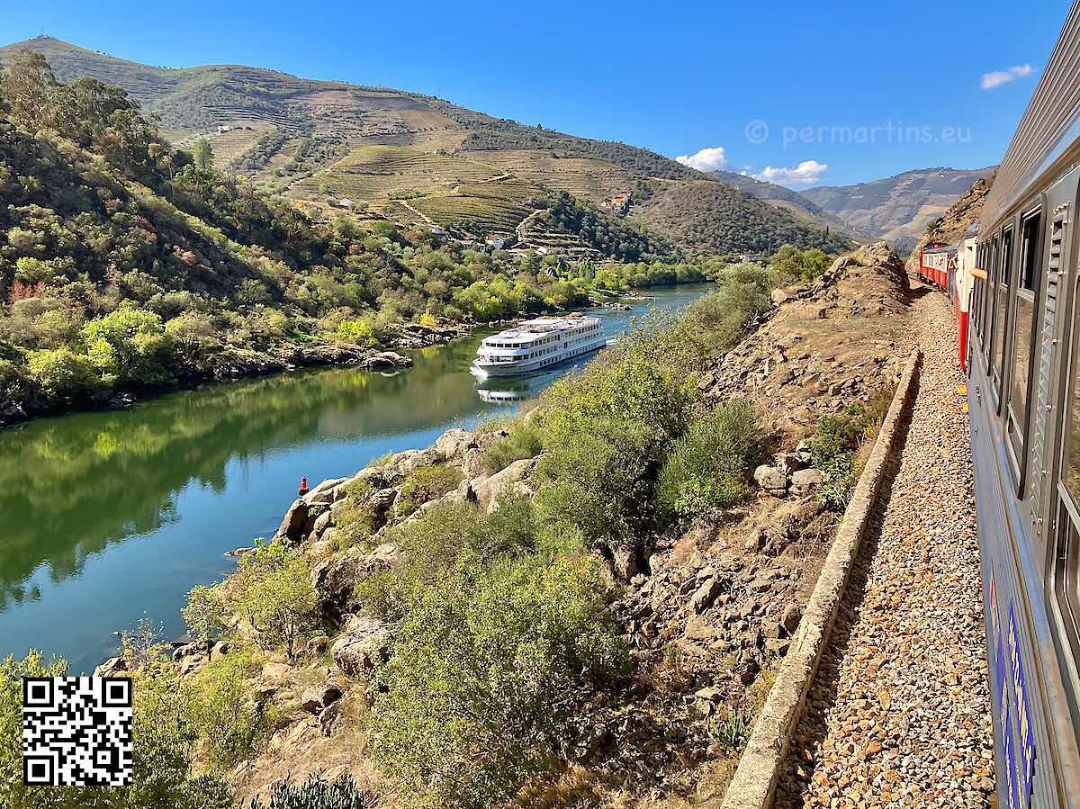 Portugal, photo from train over the Douro river with a tour boat going upstreams. Hills in the background.