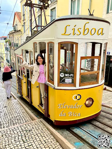 Portugal: Lisbon Lisboa Elevador da Bica yellow tram with a woman leaning outside and waving.