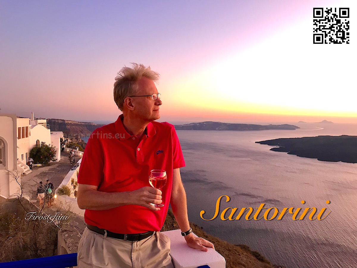 Greece Santorini Firostefani man holding a drink and looking out over the caldera at sunset.