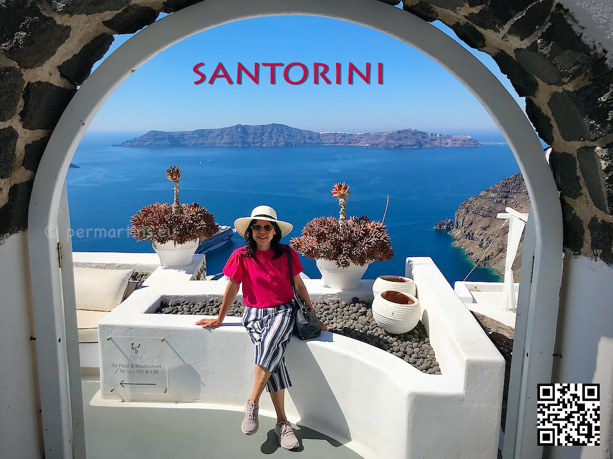 Greece Santorini Firostefani woman with a hat sitting at Dana Villas great view of caldera through an arch.