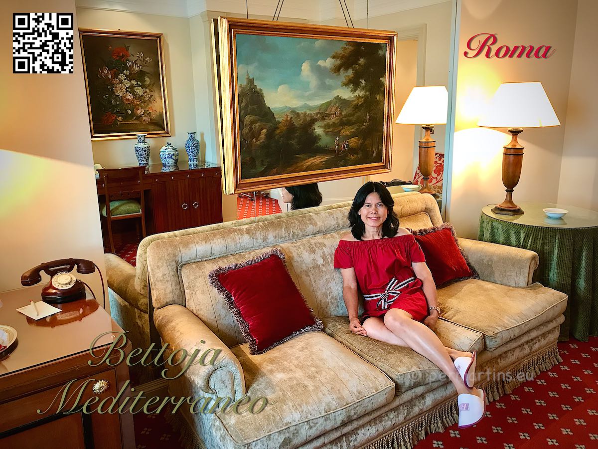 Italy Rome Hotel Bettoja woman in red dress sitting in a sofa in a suite with old paintings on the walls.