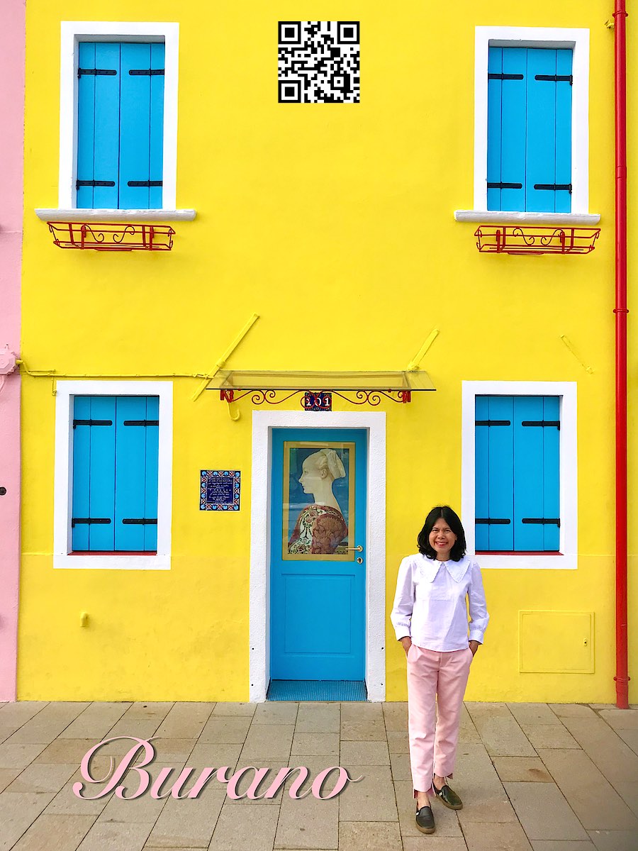 Italy Venice Burano woman standing in front of a yellow house.
