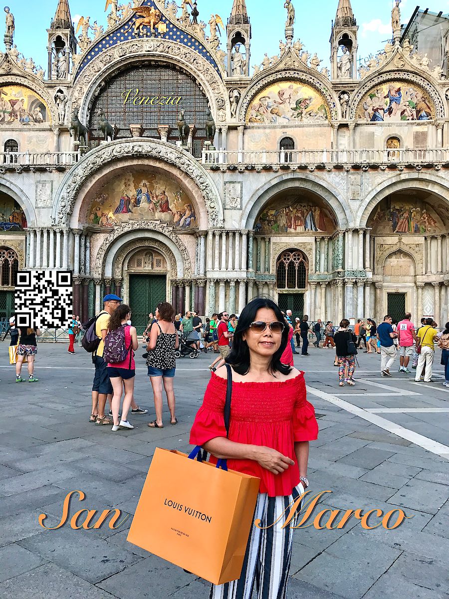 Italy Venice woman in red holding a Louis Vuitton bag at Piazza San Marco and the basilica.
